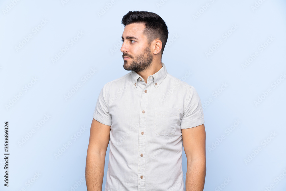 Fototapeta premium Young handsome man with beard over isolated blue background looking side