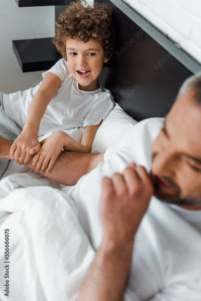 Obraz premium selective focus of curly kid looking at happy father in bedroom