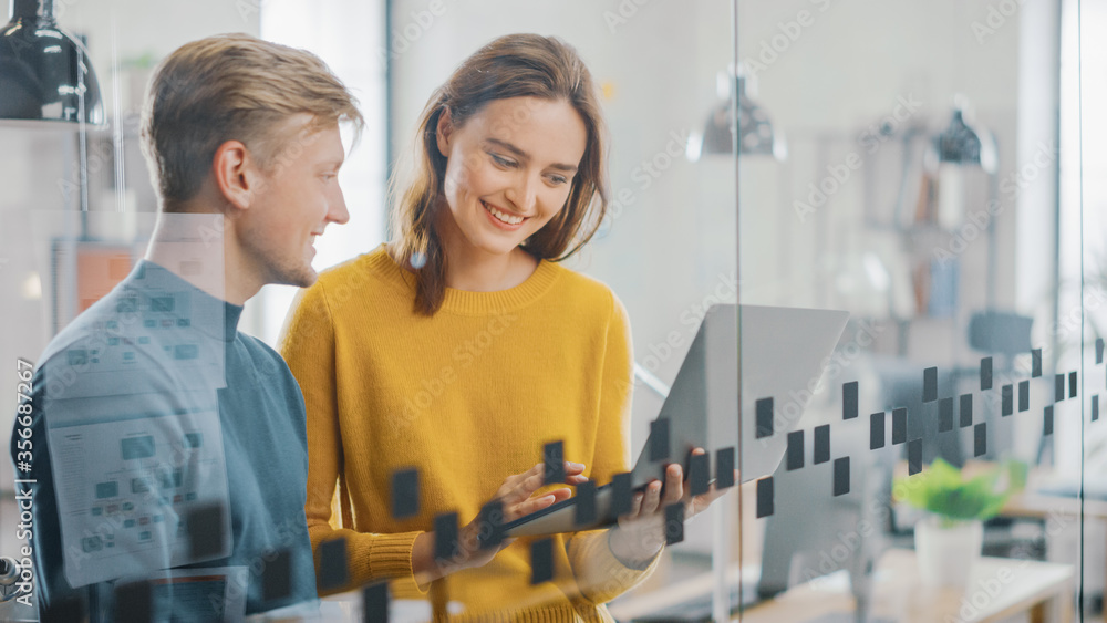 Fototapeta premium Portrait of Beautiful Young Woman Shows Laptop Display to Her handsome Male Colleague, Working on New Project. Successful Young People Working in the Modern Office.
