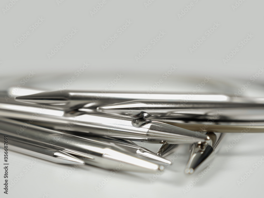 A stack of chromium metal circular knitting needles in different sizes lying on white surface, close-up shot with selective focus. A stack of chromium metal circular knitting needles in different sizes lying on white surface, close-up shot with selective focus.