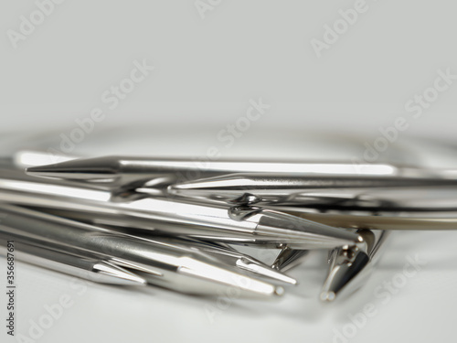 A stack of chromium metal circular knitting needles in different sizes lying on white surface, close-up shot with selective focus. 