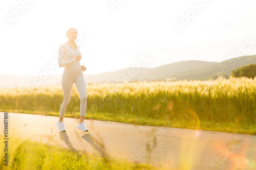 Sportliche junge Frau joggt abends zwischen Feldern photo