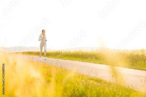 Sportliche junge Frau joggt abends zwischen Feldern