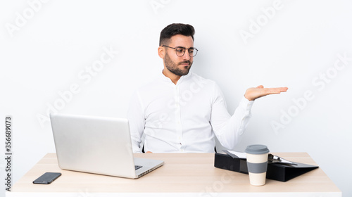 Young businessman in a workplace holding copyspace with doubts