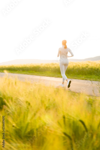 Sportliche junge Frau joggt abends zwischen Feldern © Christian Schwier