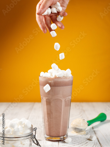Marshmallow drops in a glass of coffee on an orange background