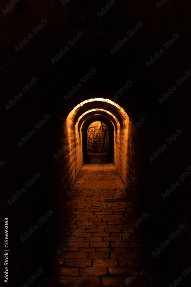 more than a century old dark paved and historic tunnel in Prague with orange light