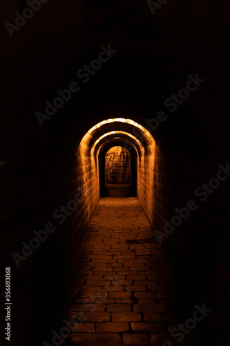 more than a century old dark paved and historic tunnel in Prague with orange light © svetjekolem
