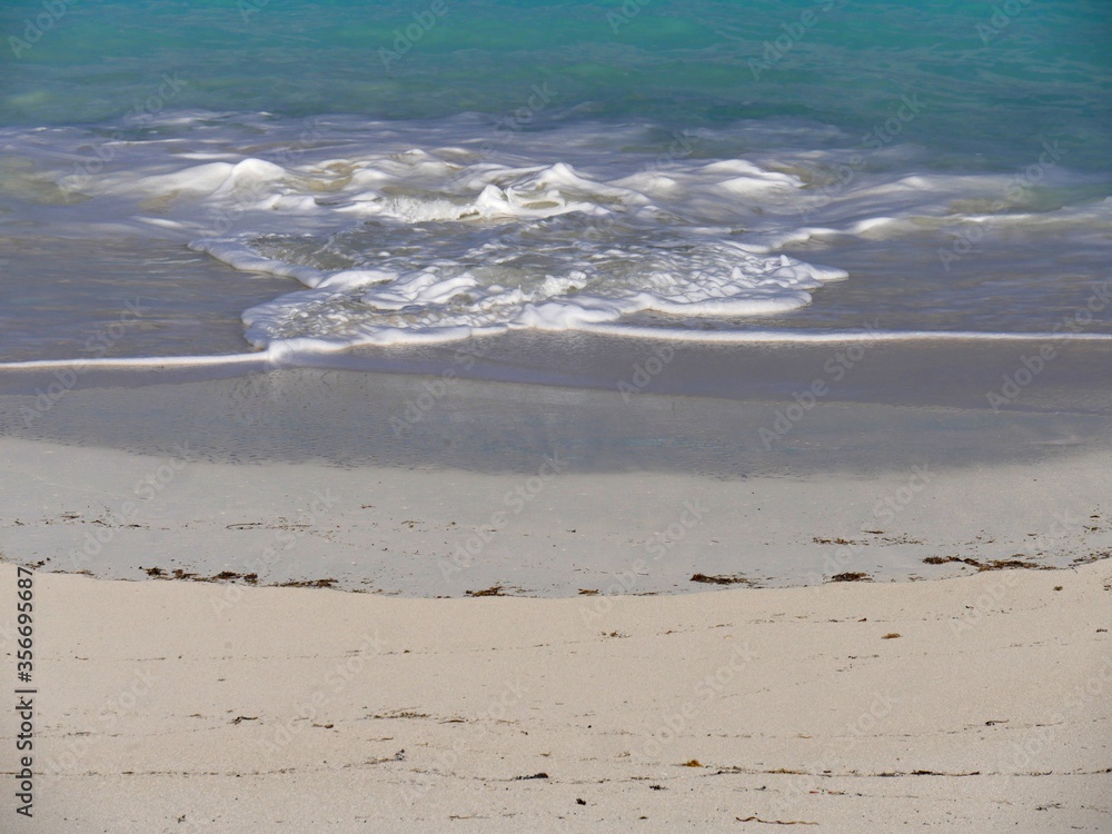 Foaming gentle waves creating patterns in the white sand beach of a tropical beach Foaming gentle waves creating patterns in the white sand beach of a tropical beach
