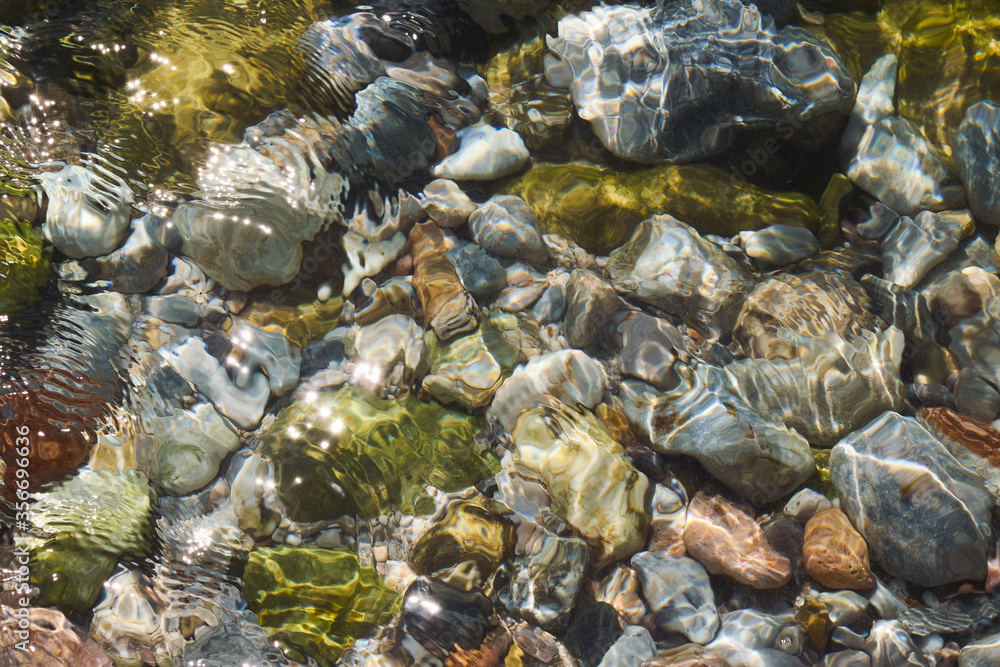 View of colorful sea pebbles by the seashore through clear transparent flowing sea water.
