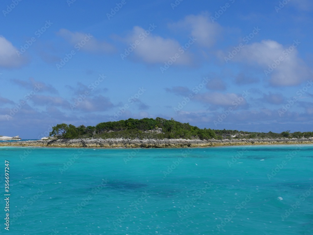 Rocky island covered in greens dotting the vast blue ocean of Bahamas in the Exuma Cays.