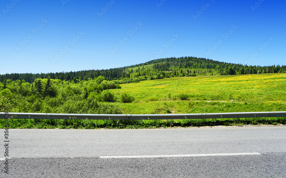 Asphalt road and green hill with trees