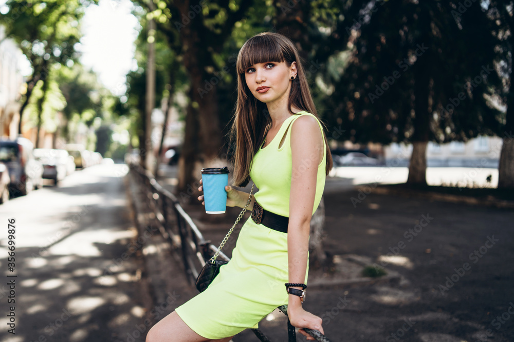 Pretty brunette girl in green dress with cup of coffee walking outdoor on the street Pretty brunette girl in green dress with cup of coffee walking outdoor on the street