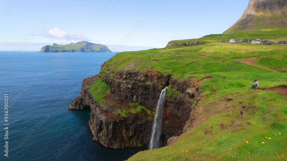 Photogtapher takes picture of Mulafossur Waterfall. Sunny summer view of Gasadalur village, Vagar, Faroe Islands, Denmark, Europe. Full HD video (High Definition).
