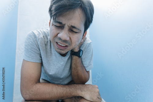 young asian man has a stomach ache sitting on a toilet bowl in the bathroom. Diarrhea