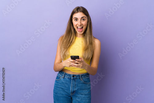 Young woman over isolated purple background surprised and sending a message