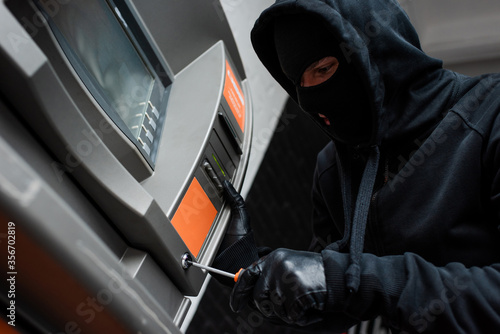 Low angle view of thief in balaclava using screwdriver while breaking atm © LIGHTFIELD STUDIOS