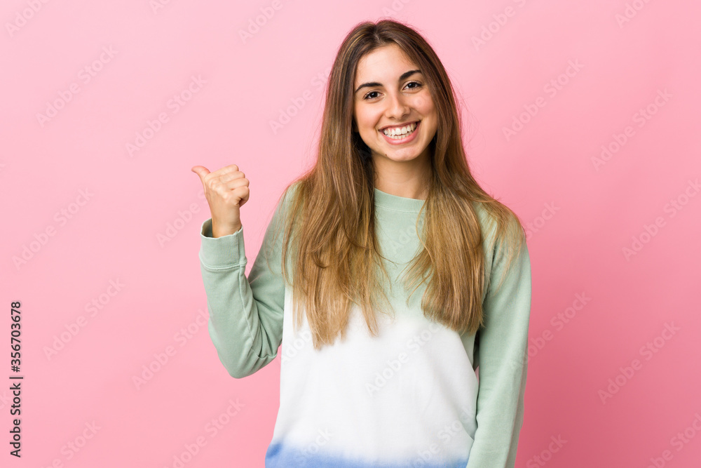 Young woman over isolated pink background pointing to the side to present a product Young woman over isolated pink background pointing to the side to present a product