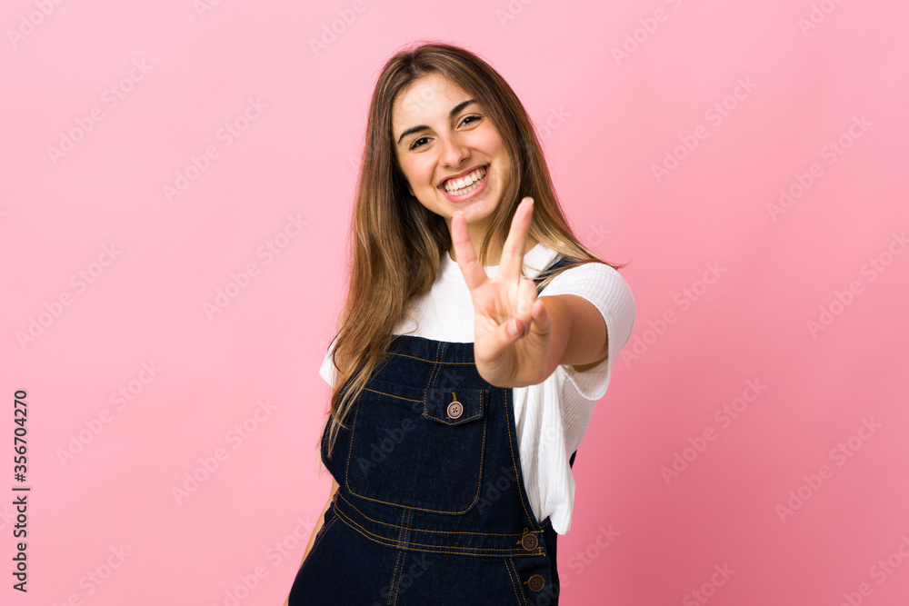 Young woman over isolated pink background smiling and showing victory sign Young woman over isolated pink background smiling and showing victory sign