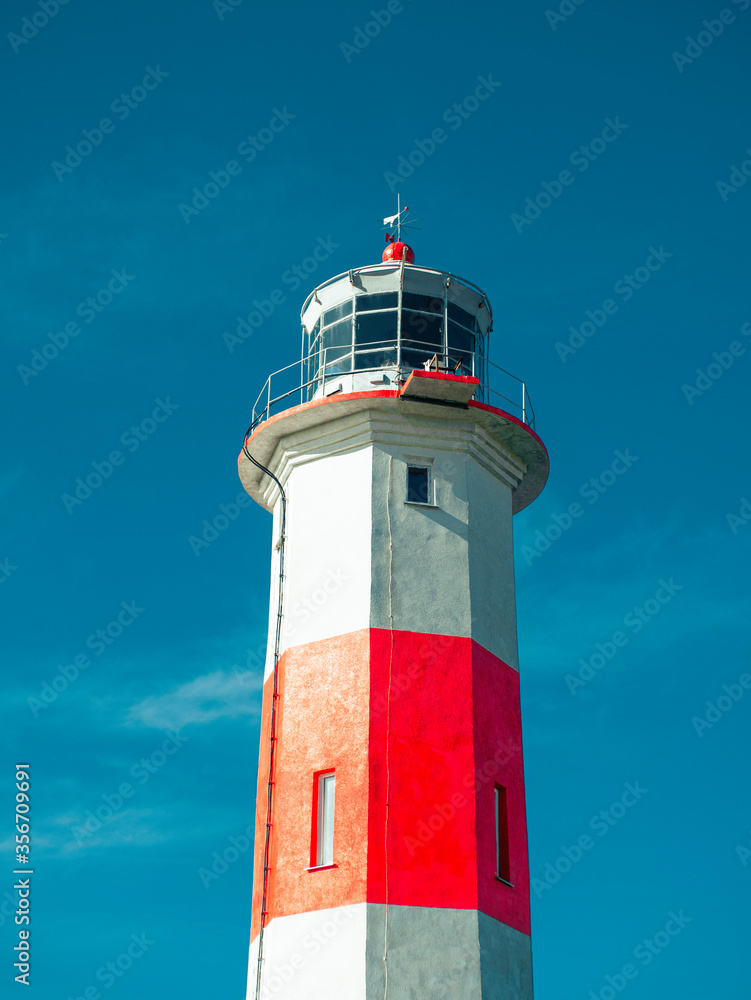 Beautiful old lighthouse, red white, isolated on blue sky background.