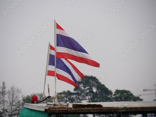 Two flags of Thailand flying from poles behind a wooden railing