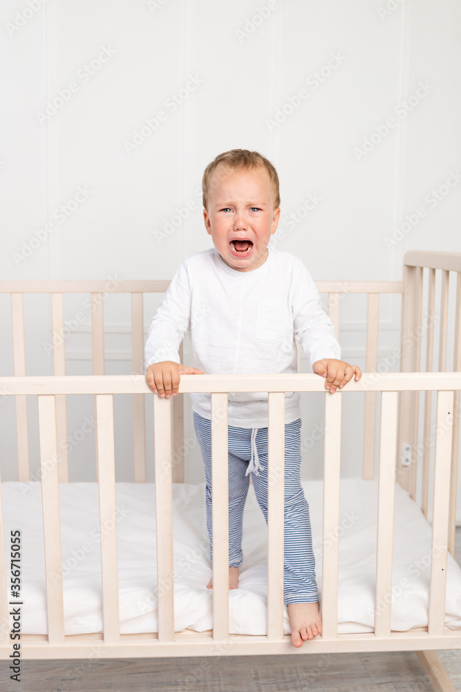 a small boy 2 years old is crying in the crib, parents do not approach the crying baby a small boy 2 years old is crying in the crib, parents do not approach the crying baby