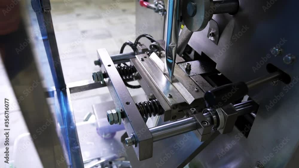 The heated mechanical metal press creates packing, working process of the metal technical device at the enterprise for packing in plastic sachets foodstuff, a side view, close-up The heated mechanical metal press creates packing, working process of the metal technical device at the enterprise for packing in plastic sachets foodstuff, a side view, close-up