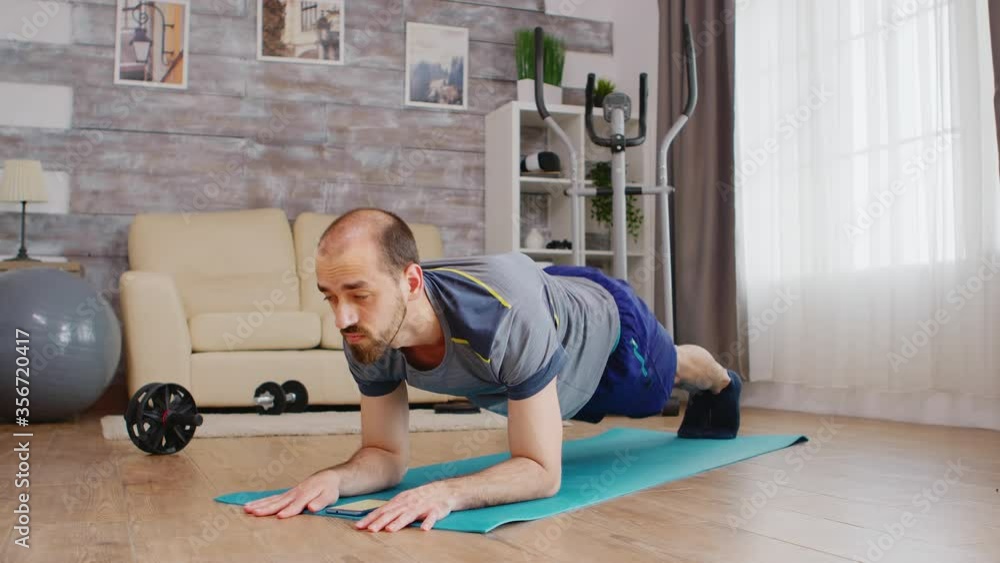 Guy press timer before doing plank workout on yoga mat at home. Sport at home and healthy lifestyle, activity, fitness and workout. Indoor training and home exercise Guy press timer before doing plank workout on yoga mat at home. Sport at home and healthy lifestyle, activity, fitness and workout. Indoor training and home exercise