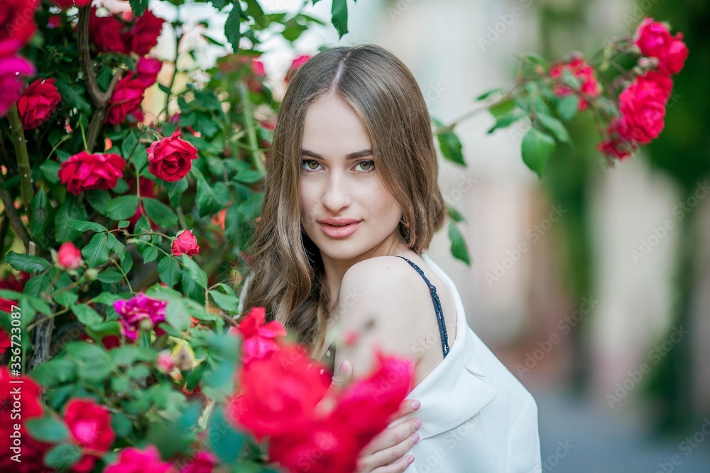 Young beautiful woman walks in a European city. Portrait of a young woman near blooming roses. Europe.