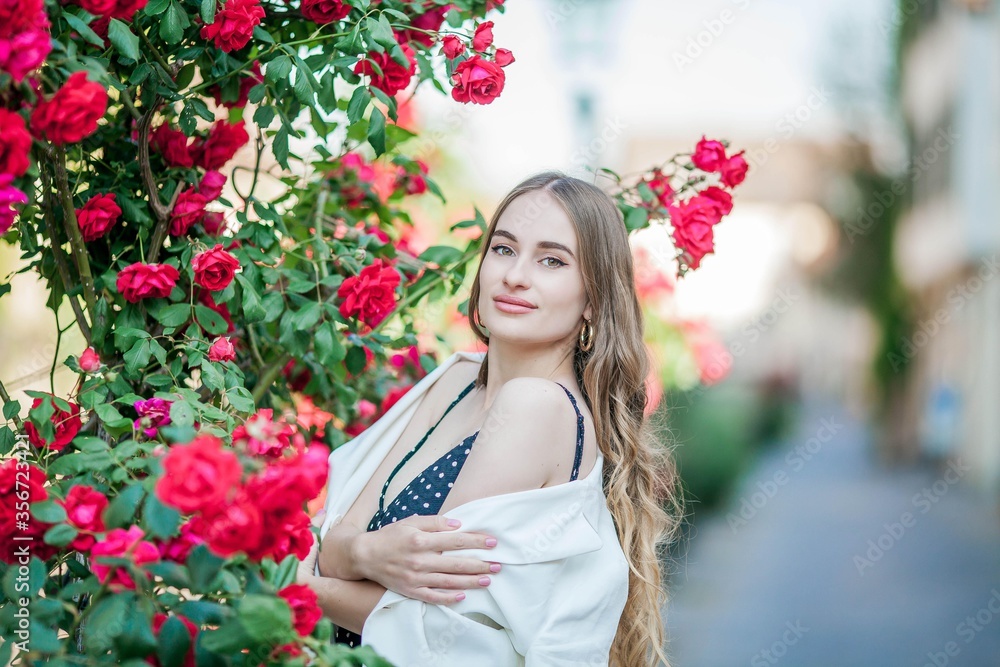 Young beautiful woman walks in a European city. Portrait of a young woman near blooming roses. Europe. Young beautiful woman walks in a European city. Portrait of a young woman near blooming roses. Europe.