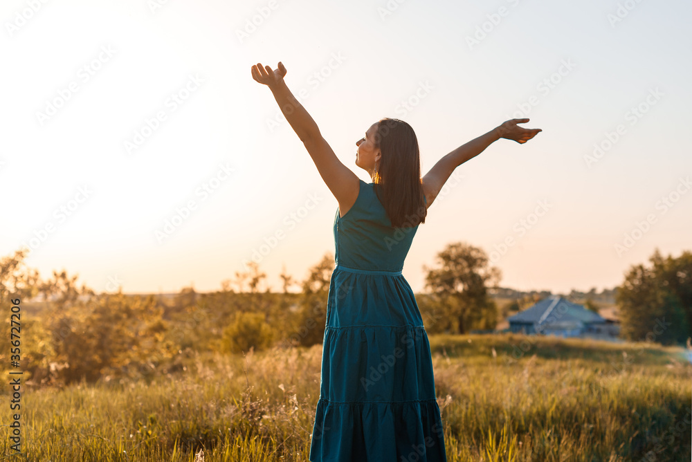 happy young woman at summer sunset in the field raises her hands to the sky happy young woman at summer sunset in the field raises her hands to the sky