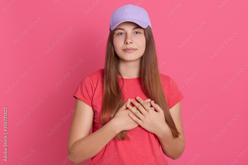Smiling young woman with hands to her chest isolated on rosy background. Close up of cheerful attractive girl looking at camera, expressing gratitude. Smiling young woman with hands to her chest isolated on rosy background. Close up of cheerful attractive girl looking at camera, expressing gratitude.