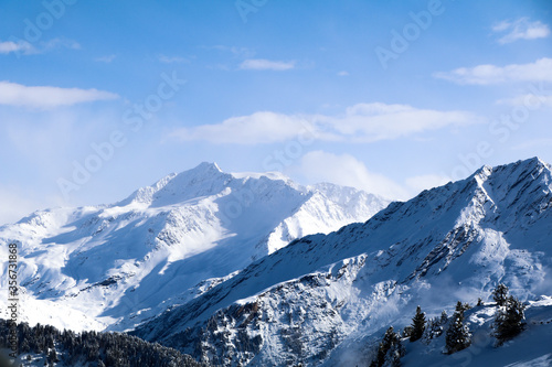 Beautiful jagged rocky mountains of the Alps with large depth of field. Trees lining the slope can be seen in the foreground covered in snow. Sunny blue-sky day. © Ben