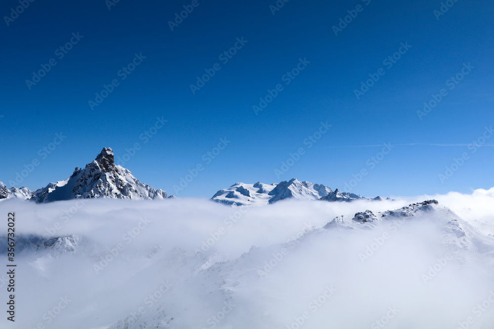 Alps mountain peaks seen in the distance appearing above a layer of cloud on a crisp sunny ski day. 