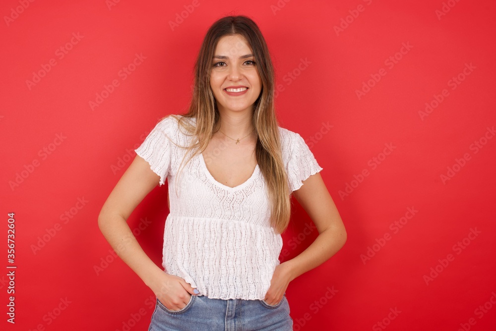 Young beautiful woman over isolated background happy face smiling with hands in pockets looking at the camera. Positive person. Young beautiful woman over isolated background happy face smiling with hands in pockets looking at the camera. Positive person.