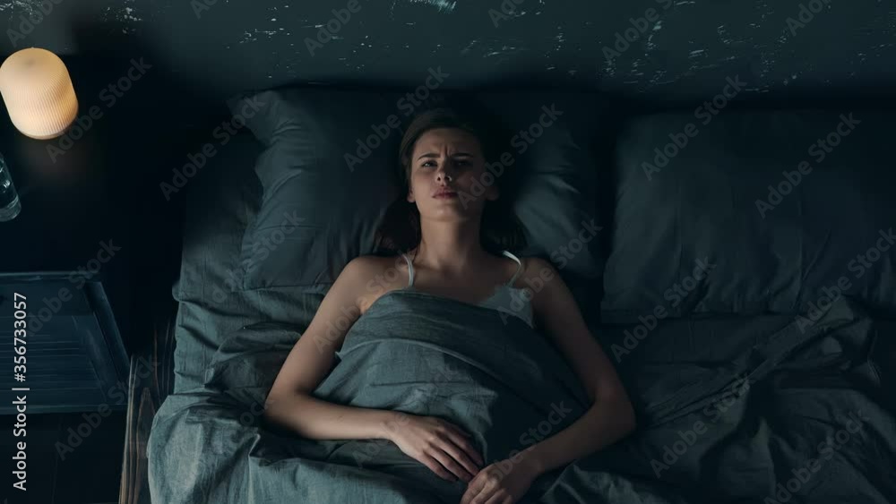 Top View of Woman Trouble Sleeping in Loft Bedroom. Beautiful Young Woman Waking up at Night and Having Bad Headache. Woman with Insomnia. Sleeping Disorder. Top View of Woman Trouble Sleeping in Loft Bedroom. Beautiful Young Woman Waking up at Night and Having Bad Headache. Woman with Insomnia. Sleeping Disorder.