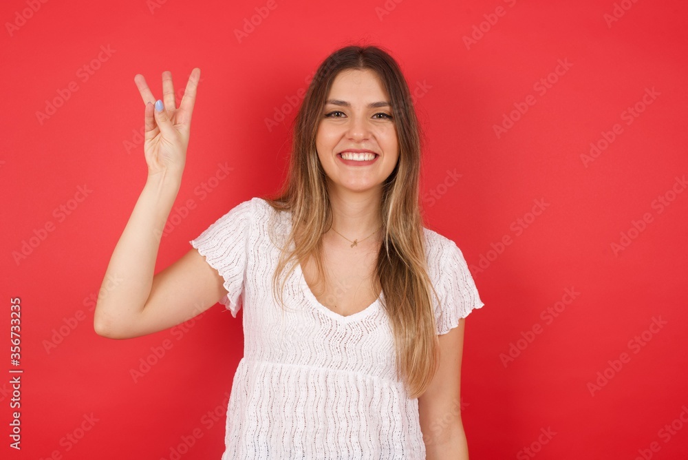 Young blonde woman standing standing against gray wall showing and pointing up with fingers number three while smiling confident and happy. Young blonde woman standing standing against gray wall showing and pointing up with fingers number three while smiling confident and happy.