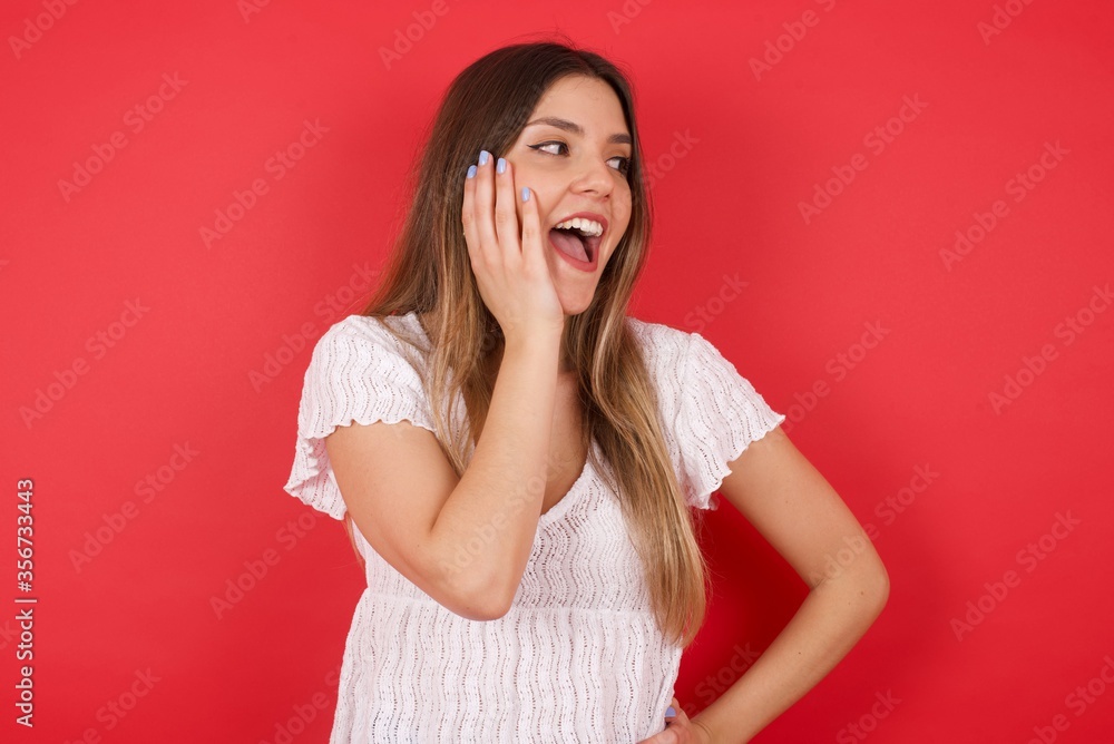 Amazement - woman excited looking to the side hand on face. Surprised happy young woman looking sideways in excitement. Caucasian female model on gray background.