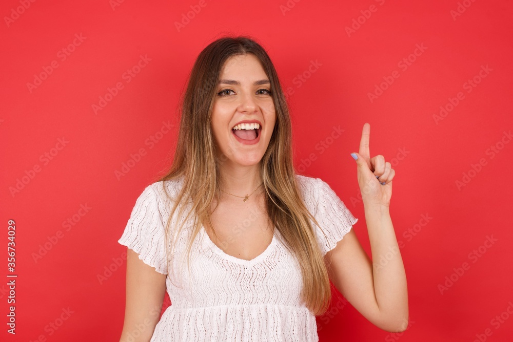 Close up portrait of pleasant looking blue eyed young woman model has clever expression, raises one finger, remembers herself not to forget tell important thing. Indoors Close up portrait of pleasant looking blue eyed young woman model has clever expression, raises one finger, remembers herself not to forget tell important thing. Indoors