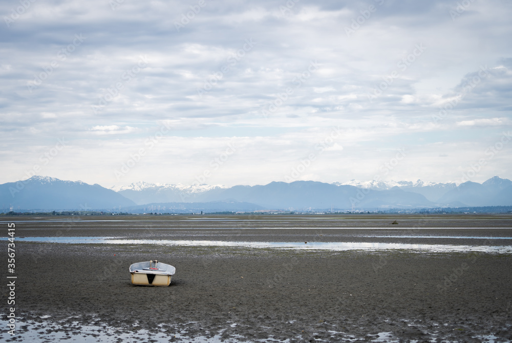 Boat siting on the ground during outflow with cloudy sky and mountains in backdrop, shot in Vancouver, British Columbia, Canada