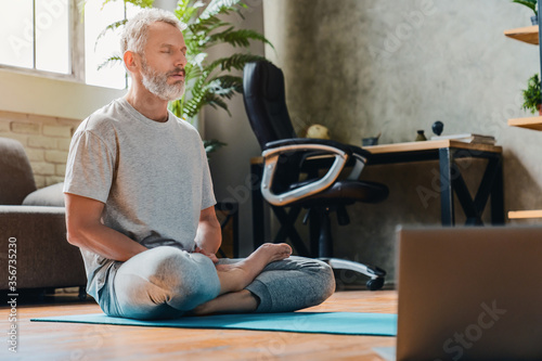 Middle aged sport man doing yoga and fitness at home using laptop