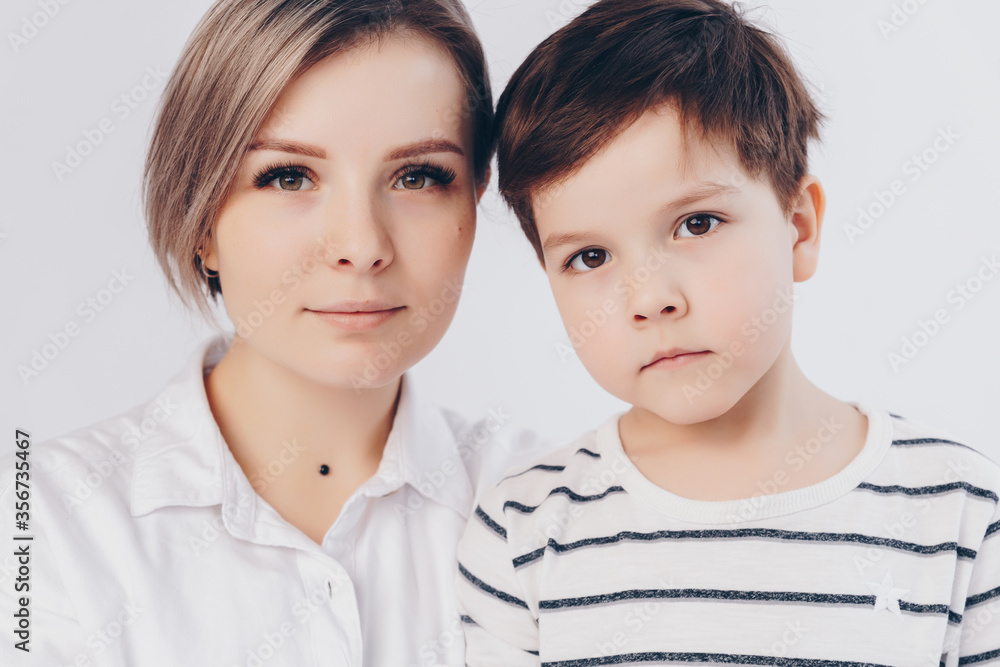 White background. Portrait of mom and son. They bow their heads to each other and look at the camera. White background. Portrait of mom and son. They bow their heads to each other and look at the camera.