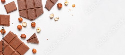 Bar and pieces of milk chocolate, hazelnut on white background flat lay top view copy space. Minimalistic Chocolate Background. Chocolate, cocoa, sweet treat, sugar, overweight, chocolate addiction