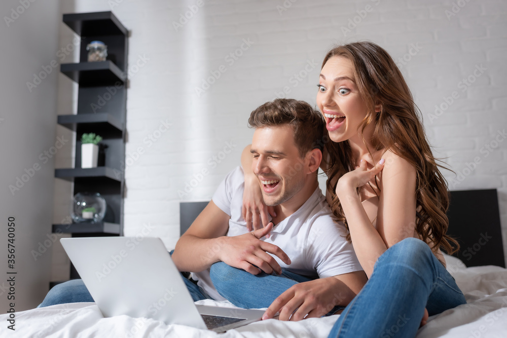cheerful woman and man laughing while watching comedy movie on laptop in bedroom cheerful woman and man laughing while watching comedy movie on laptop in bedroom