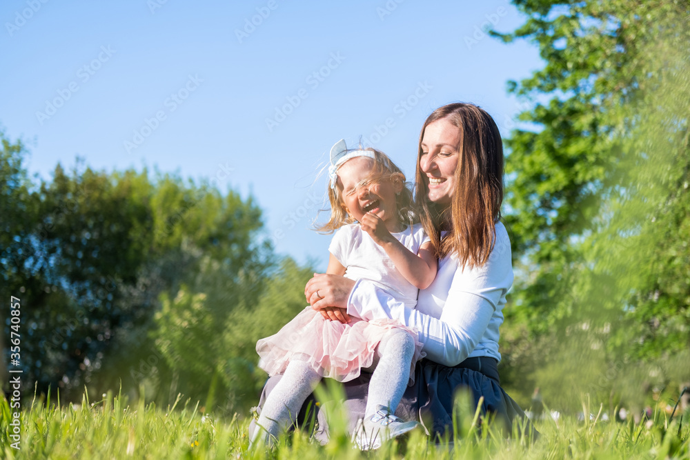 Happy mother and little daughter playing having fun outdoor in park at summer. Family lifestyle. Mom resting together on the green grass Happy mother and little daughter playing having fun outdoor in park at summer. Family lifestyle. Mom resting together on the green grass