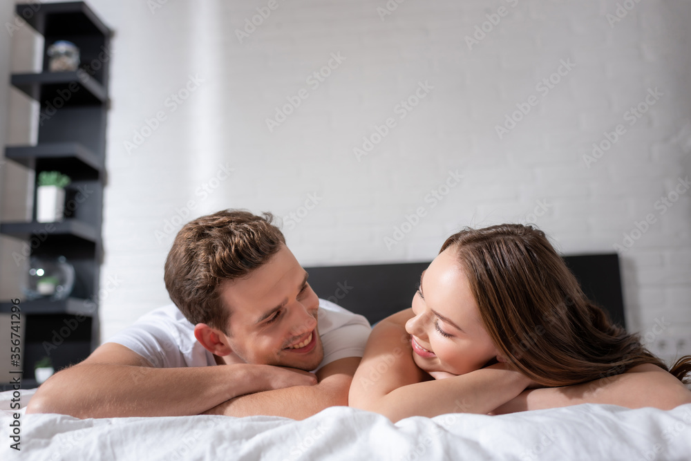 happy young couple smiling while looking at each other in bedroom happy young couple smiling while looking at each other in bedroom