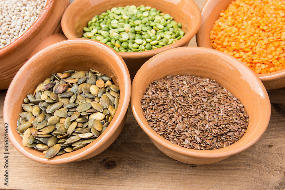 Fototapeta premium Small clay bowls with various seeds: pumpkin seeds, flaxseed, red lentils, green peas, barley grains.
