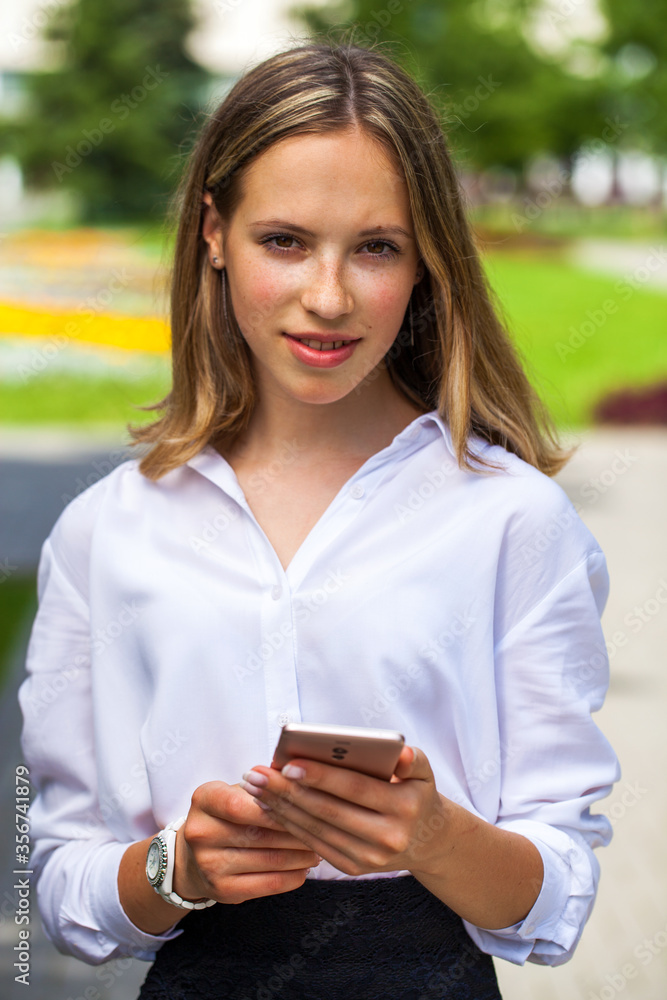 Young woman in a white blouse and with a phone in her hands posing outdoors