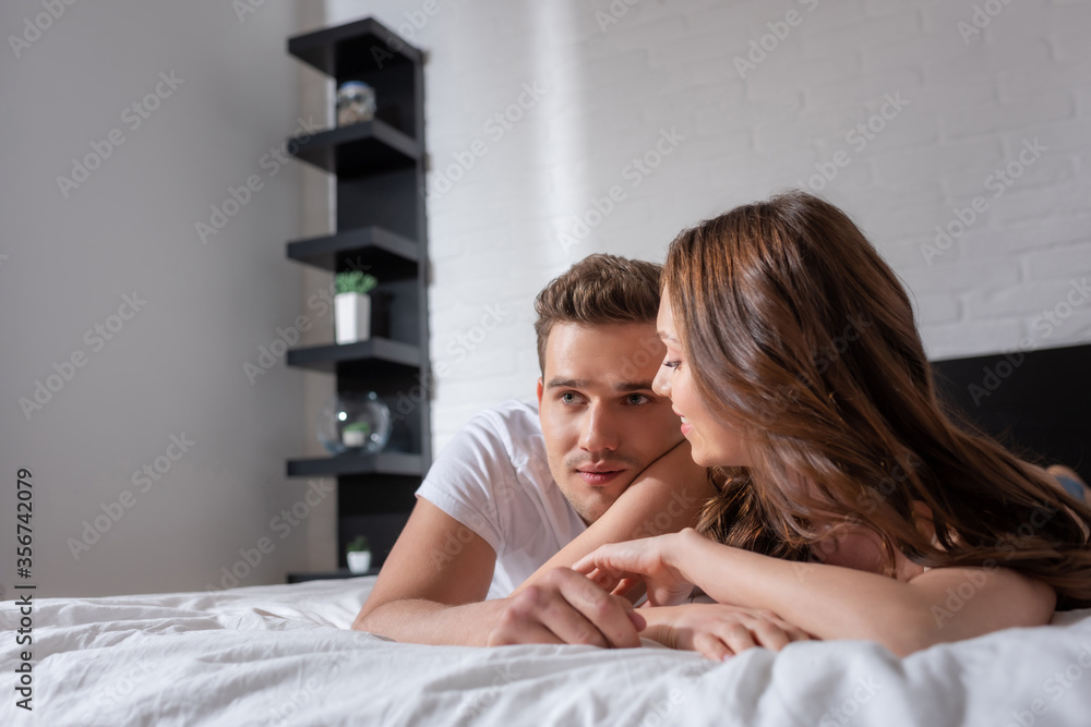 happy woman looking at handsome man lying on bed