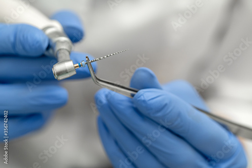 Dental tools close-up. A drill for cleaning canals in the doctor’s hand with tweezers is mounted on a mechanical drill.